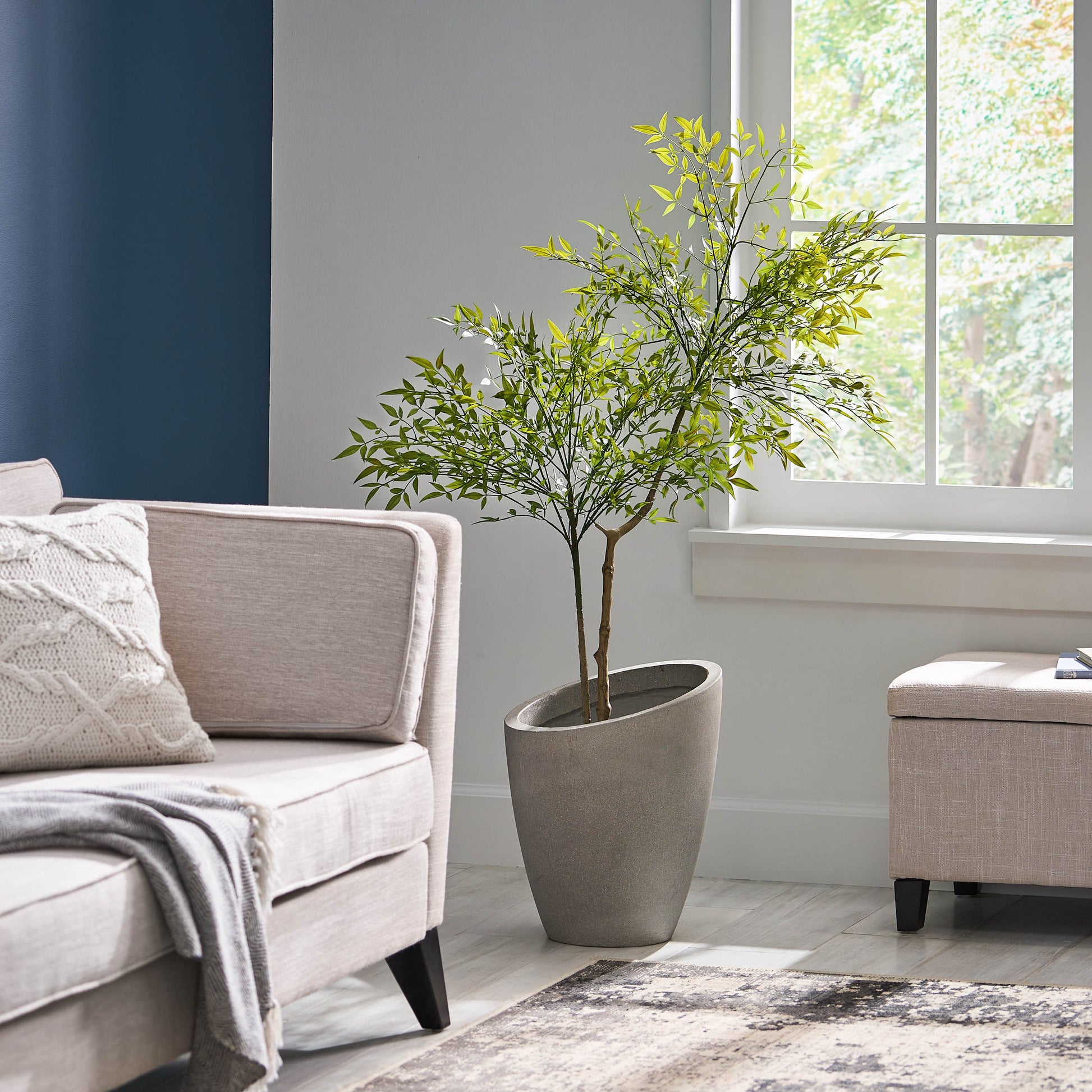 120cm artificial nandina plant in a gray pot sits in a bright living room beside a beige sofa and ottoman.