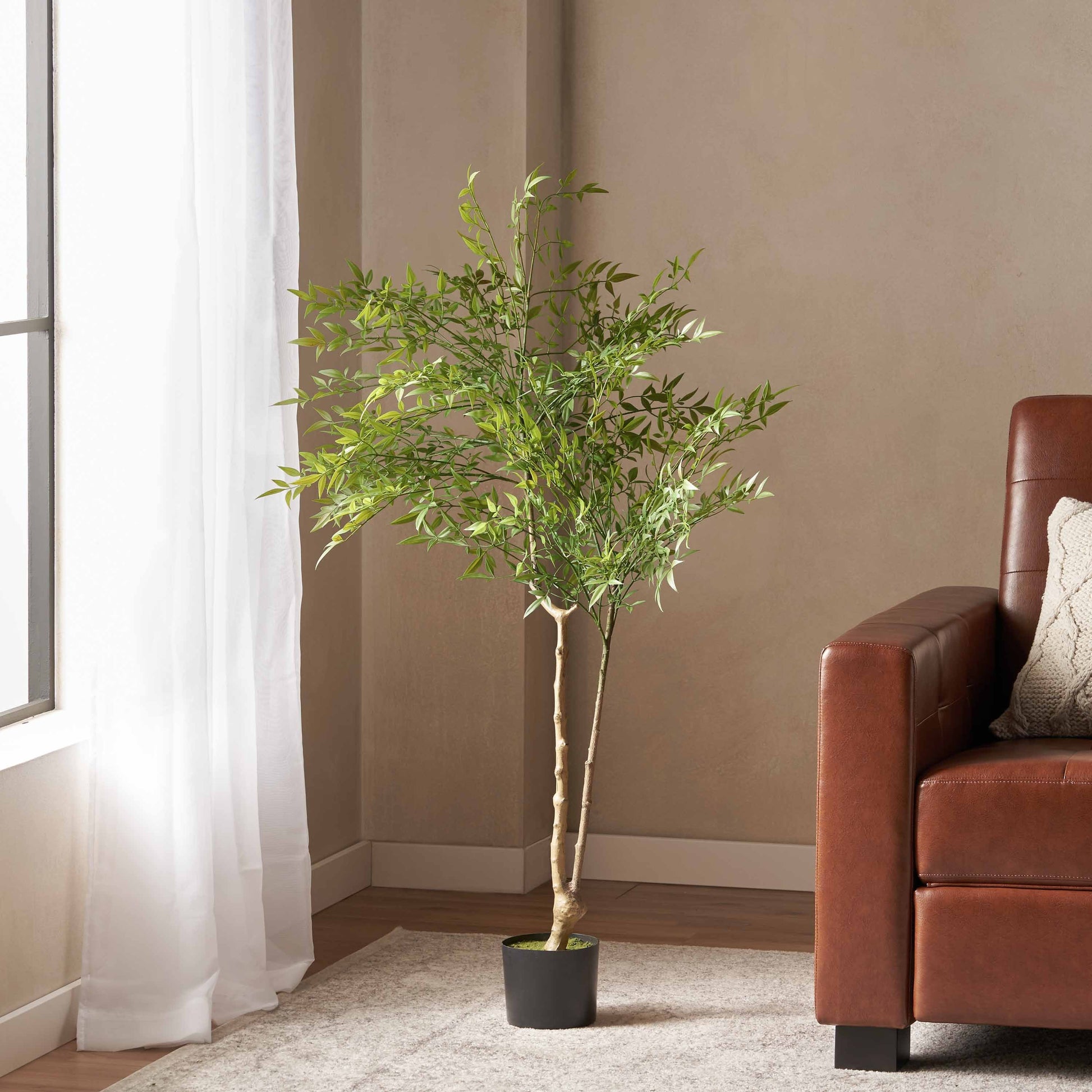 120cm artificial nandina tree with green leaves in a black pot beside a brown sofa.